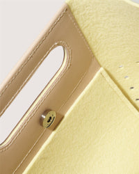Close-up of a minimalist yellow Asobi Bag by Graf Lantz, crafted from Merino wool. It features a rectangular cutout handle, metal snap button closure, and leather trim along the edge.