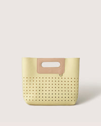 The Graf Lantz Asobi Bag is a small yellow handbag featuring perforated holes at the bottom. It includes a minimalist rectangular cut-out handle accented in beige, displayed on a simple light background.