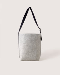 The graf lantz shoulder bag, showcased on a white background, features a grey minimalist cylindrical design crafted from water-resistant materials. It includes a black strap, subtle texture, and a small zippered opening at the top.