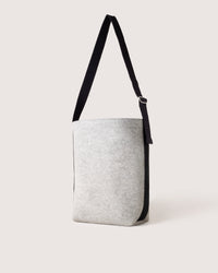 The graf lantz Merino Wool Tote features a light gray, minimalist design with a black adjustable strap. Crafted from sustainable, water-resistant materials, it stands upright against a plain white backdrop.
