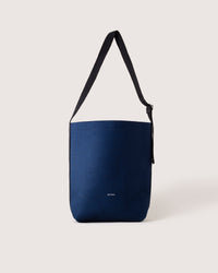 A minimalist navy blue shoulder bag from graf lantz, featuring a black strap and crafted from sustainable materials, stands out against a neutral background with a small white logo near the bottom.