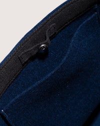 Close-up of a graf lantz blue wool garment featuring black trim and a buttoned strap. The thick, textured fabric suggests warmth and durability. The angle reveals an interior pocket and detailed stitching, highlighting its sustainable craftsmanship.