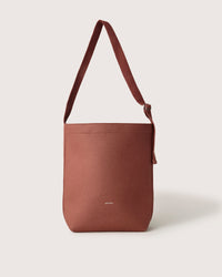 The Graf Lantz Merino Wool Tote is a brown, structured bag with a single strap and minimalist design. Good here is printed in small text on the front, all set against a plain white background, offering everyday functionality.