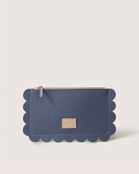 The Graf Lantz clutch showcases the Deco Edge Pouch design with a scalloped top and zipper. Made from soft Merino Wool, it features a small rectangular leather patch with text at the center, all on a plain light-colored background.