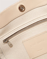 Close-up of the Graf Lantz beige Frankie Totes interior reveals a zippered pocket, structured silhouette lined with soft fabric, a leather patch with embossed text, button snap closure, and visible edge stitching.