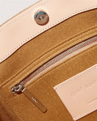 Close-up of a tan leather bags interior akin to the Frankie Tote, featuring a zippered pocket with MNL on the pull. A snap button closure sits above, while Graf Lantz is subtly embossed, making it versatile.