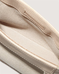 A close-up of a beige and cream open pouch, akin to the Frankie Merino Wool Clutch by Graf Lantz, showcases visible stitching. Its soft interior has a simple design without zippers or buttons, emphasizing texture and color contrast while promoting sustainable fashion.