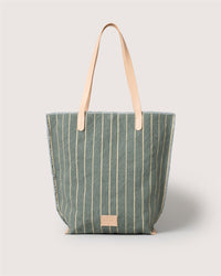 Graf Lantz striped tote with vertical cream stripes on green canvas, leather straps, and a tan leather patch on the front, shown against a plain light background.
