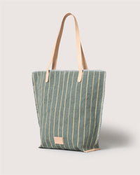 The Graf Lantz green canvas tote features vertical cream stripes, beige leather shoulder straps, and a small beige label near the bottom. Minimalist and striped, its shown against a plain light background.