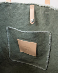 Close-up of the Graf Lantz green canvas tote bag interior, showing a stitched pocket with a tan leather patch labeled Graf Lantz and tan leather straps.