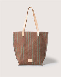 A Graf Lantz brown striped handbag with thin green vertical lines, beige leather straps, and a small beige rectangular patch near the bottom center, displayed on a plain light background.