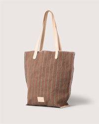 The Graf Lantz brown canvas tote features vertical green stripes, light tan leather straps, and a small rectangular label near the bottom. This striped handbag stands upright against a light, neutral background.