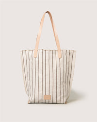 The Graf Lantz Hana Canvas Tote is a beige bag with vertical brown stripes, tan leather straps, and a small rectangular leather patch on the front, shown against a plain light background.