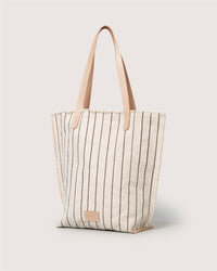 The Graf Lantz Hana Canvas Tote is a beige bag with vertical brown stripes, tan leather straps, and a small rectangular leather patch on the front, displayed against a light background.