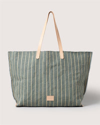 A large Graf Lantz canvas boat bag with tan leather handles, a green body with cream stripes, frayed edges, and a small brown patch near the bottom—an effortlessly versatile carryall.