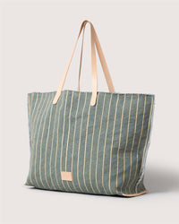 A large green canvas boat bag by Graf Lantz, featuring vertical beige stripes, beige leather handles, and a small rectangular leather patch on the front—an everyday versatile carryall displayed against a light background.