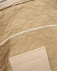 Close-up of a tan fabric pocket with visible stitching and a beige Vachetta leather patch embossed with Graf Lantz. A silver zipper at the top highlights the refined craftsmanship, making this piece a standout accessory in any shoulder bag collection.