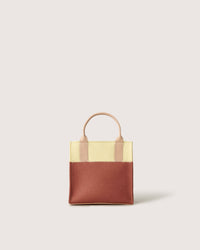 A small Graf Lantz two-toned mini tote handbag features a yellow upper section, a brown lower section, and a short beige handle against a plain light background.