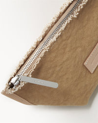 Close-up of the Graf Lantz Hana Canvas Pouch showcases its textured surface and metallic zipper with an engraved brushed metal pull. Featuring artisanal fraying along its soft, furry border at the zipper seam, it is part of the Hana totes collection.