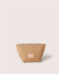 A small, light brown Graf Lantz Hana Canvas Pouch with a rectangular leather patch on the front is displayed against a pale background, highlighting its elegant simplicity and subtle artisanal fraying.