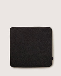 A view from above of a square, dark gray Zabuton seat cushion by graf lantz, against a light background. This cushion, made with soft Merino wool, has rounded corners and a textured fabric surface.