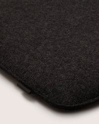 A close-up of a dark gray felt fabric with smooth texture shows rounded edges and a small black tag by graf lantz. Crafted from fine Merino wool, this elegant piece mirrors the serenity of Zabuton Seat Cushions against a calming light cream background.