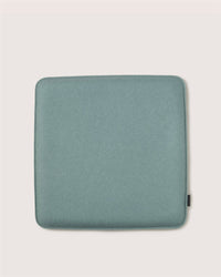 A square, teal meditation cushion by Graf Lantz with rounded corners and a small black fabric tag on the right edge, placed on a plain light background.