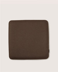 A square, dark brown Graf Lantz cushion with rounded corners sits on a light beige background. Its surface looks soft and smooth.