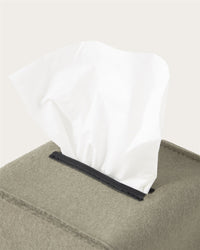 A close-up of a white tissue partially pulled from a gray Graf Lantz Merino wool tissue box cover, set against a plain light background—ideal for minimalist home décor.