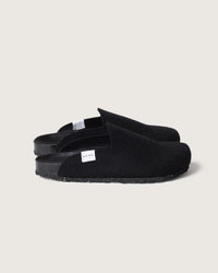 The graf lantz black slip-on slippers boast a minimalist design with a small white side label, crafted with recycled rubber soles and a soft fabric upper, set against a light gray background.