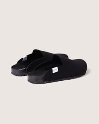 Graf Lantz slip-on sandals in black, featuring a closed-toe design with a fabric exterior. They sport a recycled rubber sole, flat footbed, and a label on the side of each sandal. Displayed on a plain background.