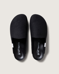 A pair of minimalist black slip-on shoes in Merino wool felt, featuring graf lantz insoles and recycled rubber soles, are positioned side by side against a light gray background.