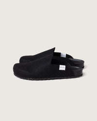 Graf lantz black slip-on clogs are set against a light grey background, highlighting their Merino wool felt texture and black soles made from recycled rubber, with a small white tag adorning the side.