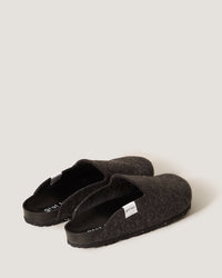 A pair of dark gray woolen slipper shoes by graf lantz, featuring black soles, lies on a light gray surface. Made from sustainable Merino wool felt, these casual slip-ons include a small white tag on each side, effortlessly combining comfort and style.