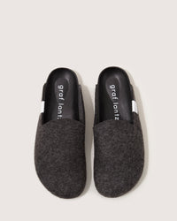 These gray slippers by graf lantz, made of Merino wool felt, have a minimalist design with black insoles, closed toes, and open backs, exemplifying sustainable footwear on a plain light background.