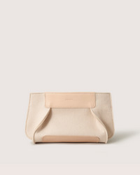 Introducing the Graf Lantz Merino Wool Clutch, a stylish cream-colored accessory with a minimalist design. Crafted from sustainable materials, it features subtle brand engraving and tan accents for an elegant look, showcasing the benefits of Merino wool against various backdrops.