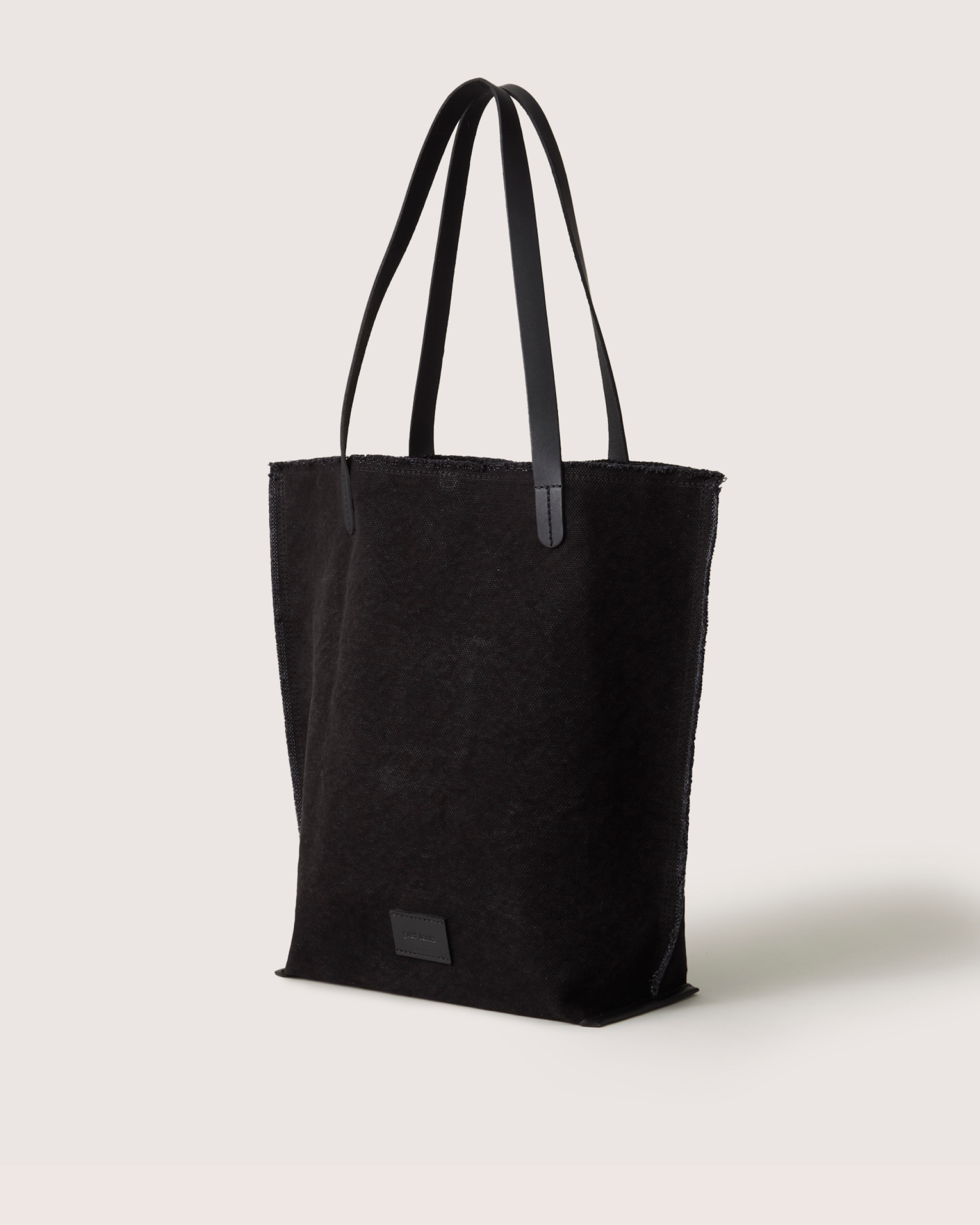 The Graf Lantz black tote bag, made from durable cotton canvas, showcases long, slim handles on a neutral backdrop. Its minimalist design is enhanced by a small rectangular label near the base.