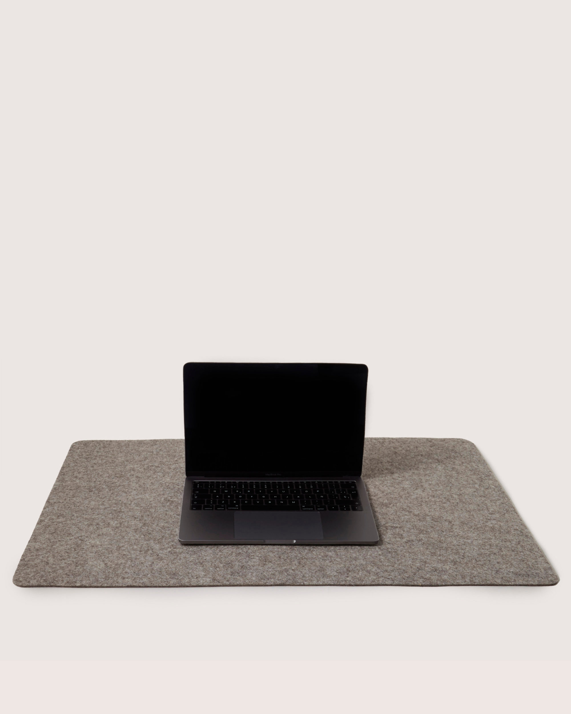 A laptop with a black screen rests on the spacious Graf Lantz Mosen Desk Pad, crafted from premium Merino Wool. The large, rectangular gray felt mat enhances this serene workspace against a plain light background.
