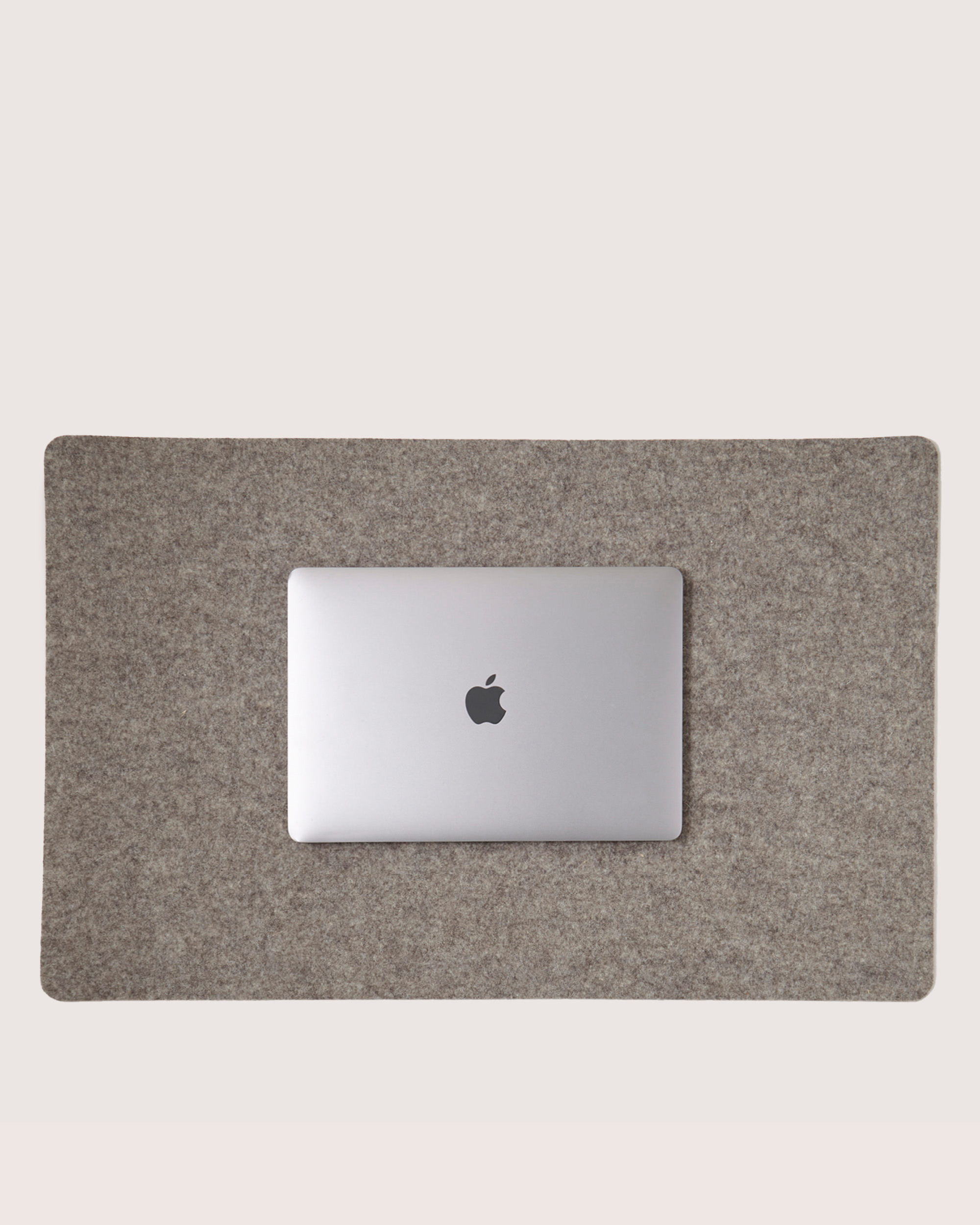 A silver laptop with an Apple logo sits on a Graf Lantz desk pad, made of soft Merino wool, against a plain white background.