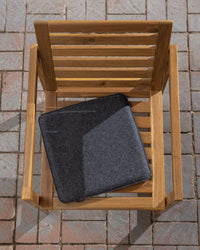 A graf lantz wooden chair featuring a gray Merino wool cushion sits on a paved brick surface, with sunlight casting sharp shadows that create a warm and inviting atmosphere ideal for meditation.