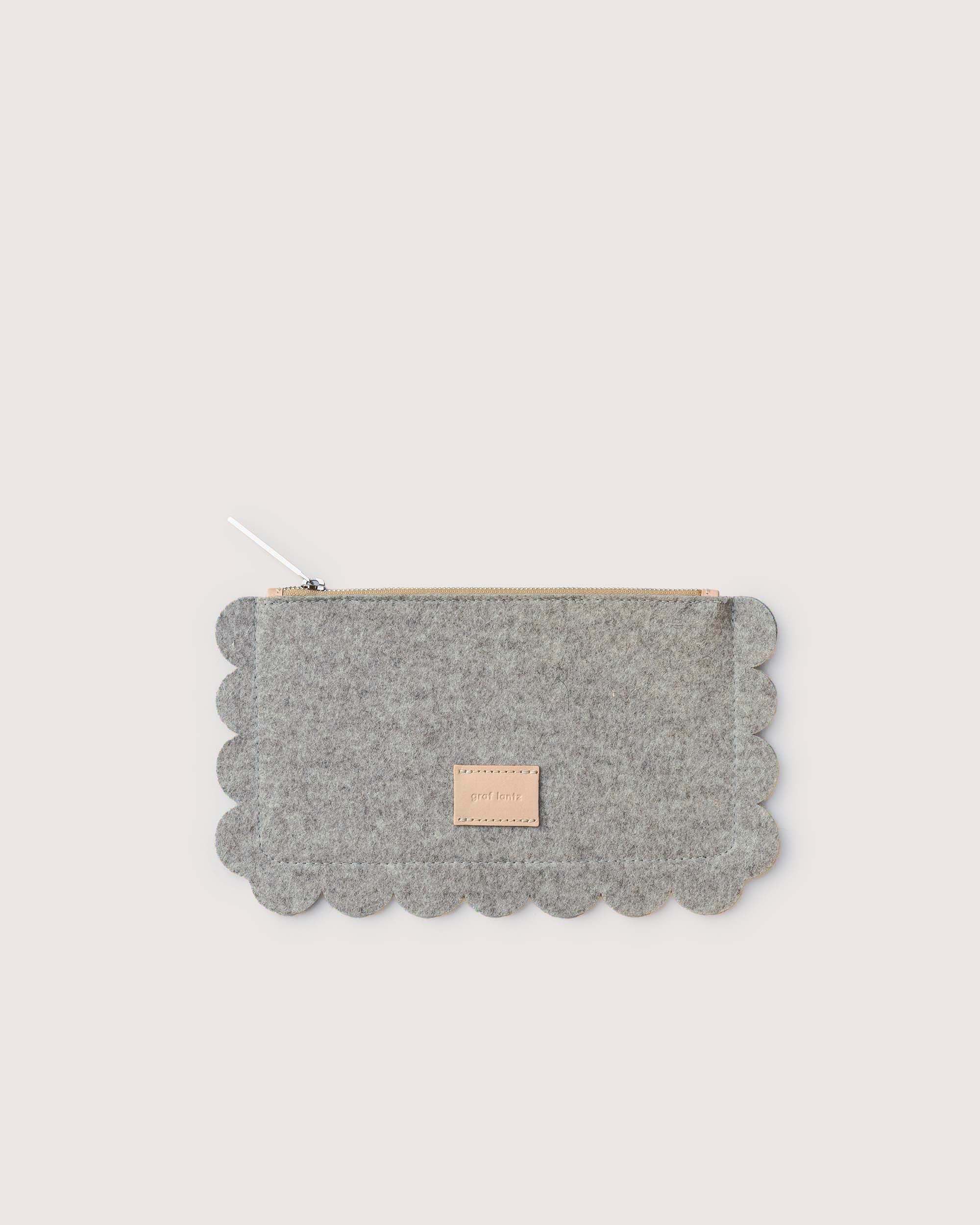 The graf lantz Deco Edge Pouch in gray is made from sustainable Merino wool felt, boasting scalloped edges and a top zipper. A small rectangular label accents one side against a plain light background.