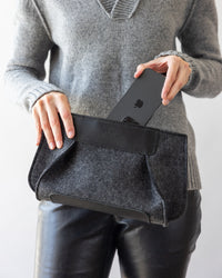 A woman taking a mobile phone out of a charcoal Frankie Merino Wool Clutch