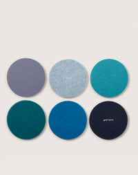 Six round felt Merino wool coasters in blue and teal are arranged in a Kobon leather tray. One coaster in the bottom row features the graf lantz logo. The entire set is beautifully crafted by hand in Los Angeles.