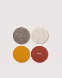 Graf Lantzs Perfect Beer Felt features four round Merino wool coasters arranged in a square: a gray and cream coaster on top, an orange coaster, and a red with white text below, all on a light background. Ideal for any decor.