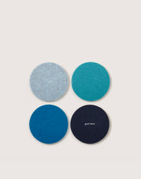 Four round coasters, made from premium German Merino wool in various blue shades, are arranged in a square on a light background. The bottom right coaster displays the brand name, graf lantz.
