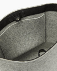 The graf lantz grey felt tote bag is made from sustainable materials, featuring black trim and a small front interior pocket for functionality. It has a button clasp to secure the top, and its soft fabric makes it perfect for daily use.