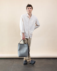 A person stands against a plain background wearing a light shirt, khaki pants, and dark slippers, holding a graf lantz grey Merino Wool Tote with a black handle, highlighting its everyday functionality and sustainable design.