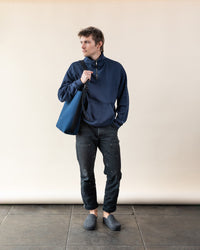 Against a neutral backdrop, someone in a navy pullover and dark pants carries a graf lantz sustainable Merino Wool Tote. They embody everyday functionality and wear gray slippers, looking to the side with a relaxed posture.