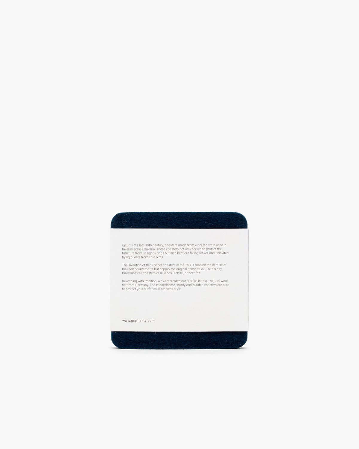 A square coaster with a white paper top and dark base on a plain background features text about the sustainable use of Canadian tree pulp. Created by graf lantz, this eco-friendly coaster highlights the history of using renewable resources.