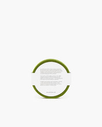 A green circular object from graf lantz, akin to a coaster, bears a white paper label wrapped around it. Mystery shrouds its purpose due to partially legible text. Set against a plain white background, the item sparks curiosity and intrigue.